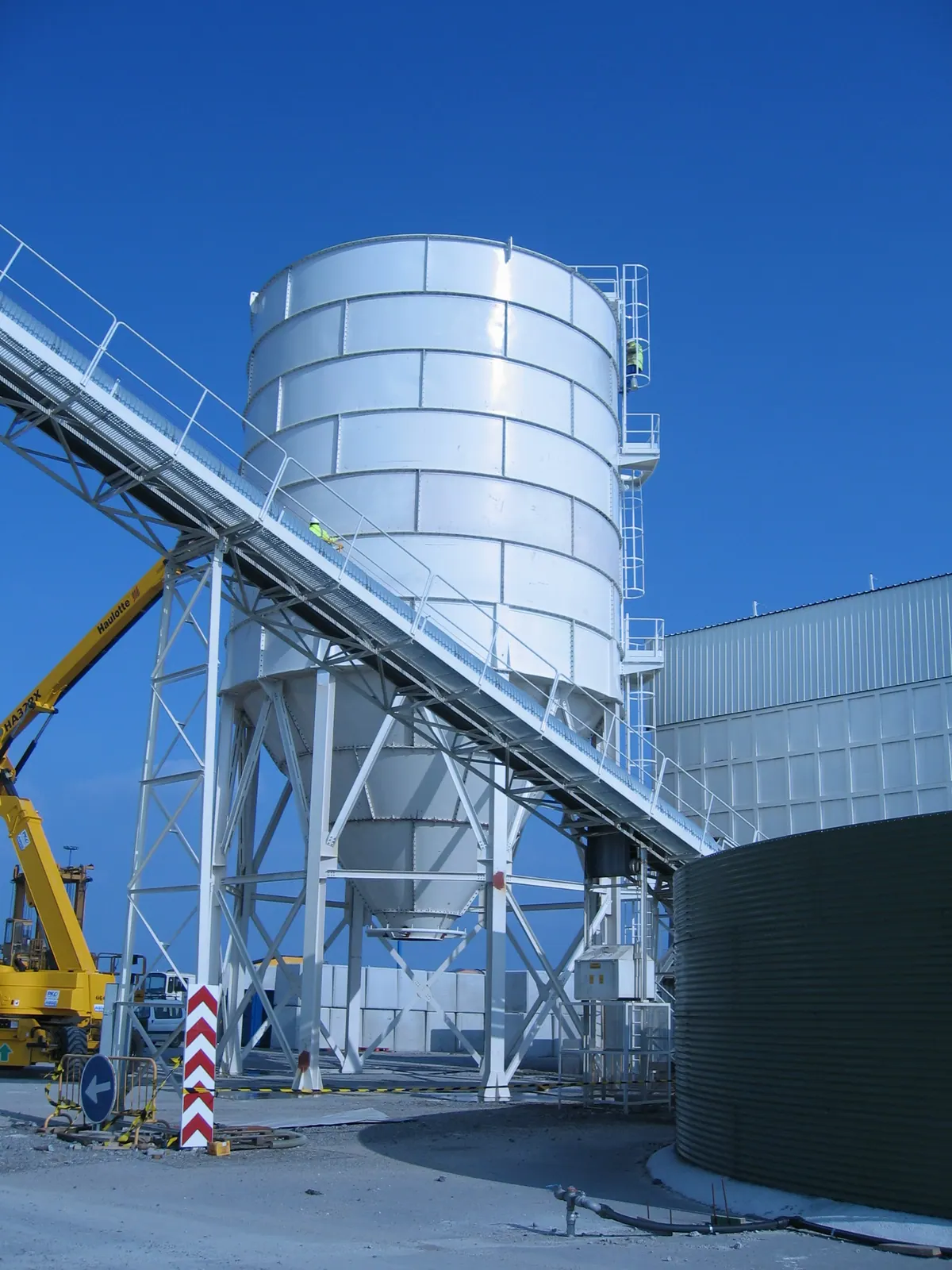 Silo de almacenamiento sobre estructura elevada con cinta transportadora, montado en planta